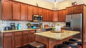 A modern kitchen with wooden cabinets, stainless steel appliances, a granite countertop, and a bar stool area.