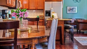 A wooden dining table with a vase of pink flowers, surrounded by chairs.