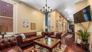 A spacious living room with a leather sofa, a glass coffee table, and a chandelier.