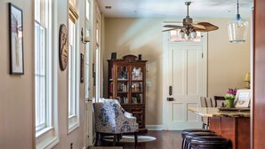 A hallway with a patterned armchair, a wooden bookcase, and a bar area with stools.
