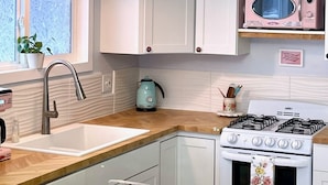 A modern kitchen with white cabinets, a stainless steel sink, a gas stove, and a unique circular light fixture.