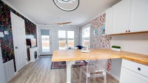 A kitchen with a wooden countertop, clear plastic chairs, white cabinets, and a ceiling fan.