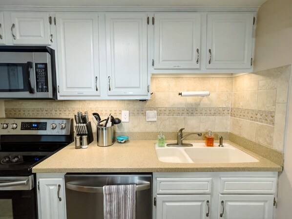 A kitchen with white cabinets, a stainless steel microwave, a built-in oven, a sink with a faucet, and a dish rack. - Beautiful 2bd/2ba Condo w/Full Kitchen Close To Everything in Myrtle Beach! (Myrtle Beach)