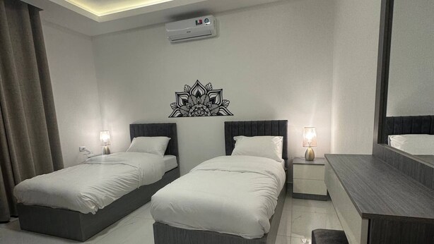 A modern hotel room with two beds, a large mirror, a vanity, and an air conditioning unit.