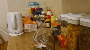 Uma bancada de cozinha com diversos alimentos e recipientes, incluindo uma chaleira branca, um pão e potes de condimentos.