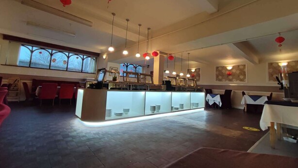 Um restaurante espaçoso com teto alto, iluminação pendente e uma ilha central com frente de vidro.