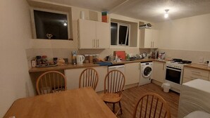 Uma cozinha compacta com mesa, cadeiras, máquina de lavar e fogão.