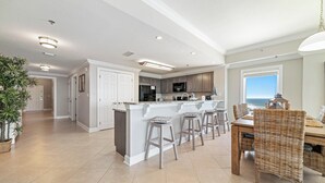 A spacious kitchen with a central island, bar stools, and a dining area with a wicker chair. - Spacious, luxury condo on the water, with a beautiful view, conveniently located (Orange Beach)
