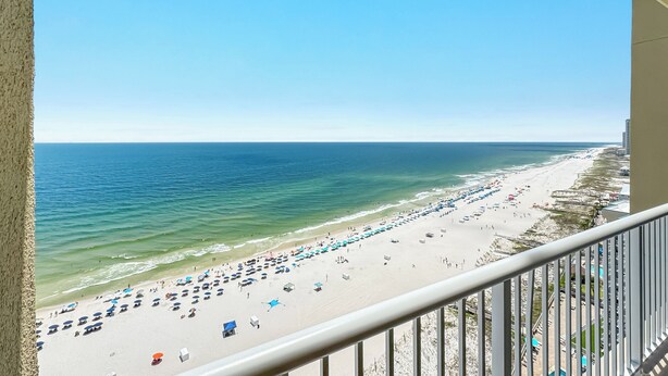 A beach view from a balcony with a railing, ocean, and beach umbrellas. - Spacious, luxury condo on the water, with a beautiful view, conveniently located (Orange Beach)