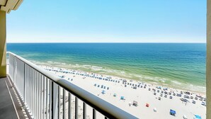 A balcony with a view of a beach with umbrellas and people. - Spacious, luxury condo on the water, with a beautiful view, conveniently located (Orange Beach)