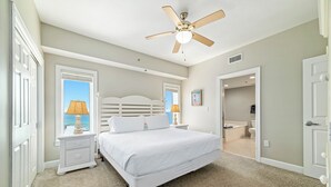 A bedroom with a bed, nightstands, a ceiling fan, and a view through a window. - Spacious, luxury condo on the water, with a beautiful view, conveniently located (Orange Beach)