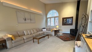 A living room with a beige sofa, a coffee table, a fireplace, and a large window. - Ski Retreat Townhome in Plymouth, VT (Plymouth)