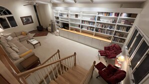 A spacious living room with a large bookshelf, a fireplace, and a staircase leading to an upper level. - Ski Retreat Townhome in Plymouth, VT (Plymouth)
