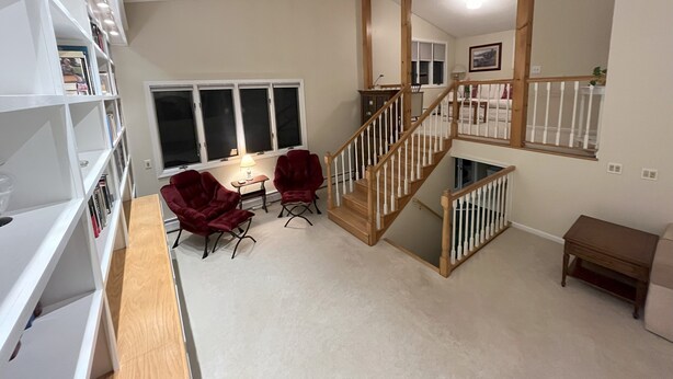 A spacious room with a wooden staircase, a bookshelf, a desk with two chairs, and a window with blinds. - Ski Retreat Townhome in Plymouth, VT (Plymouth)