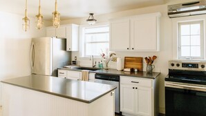 A modern kitchen with white cabinetry, stainless steel appliances, and pendant lighting. - Downtown Historic Home / Full Kitchen / W/D / Coffee, Tea, Cold Drinks, Snacks (Moscow)