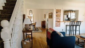 A staircase with white balusters, a dining area with a table and chairs, a blue sofa, and a kitchen area with a brick wall and hanging lights. - Downtown Historic Home / Full Kitchen / W/D / Coffee, Tea, Cold Drinks, Snacks (Moscow)