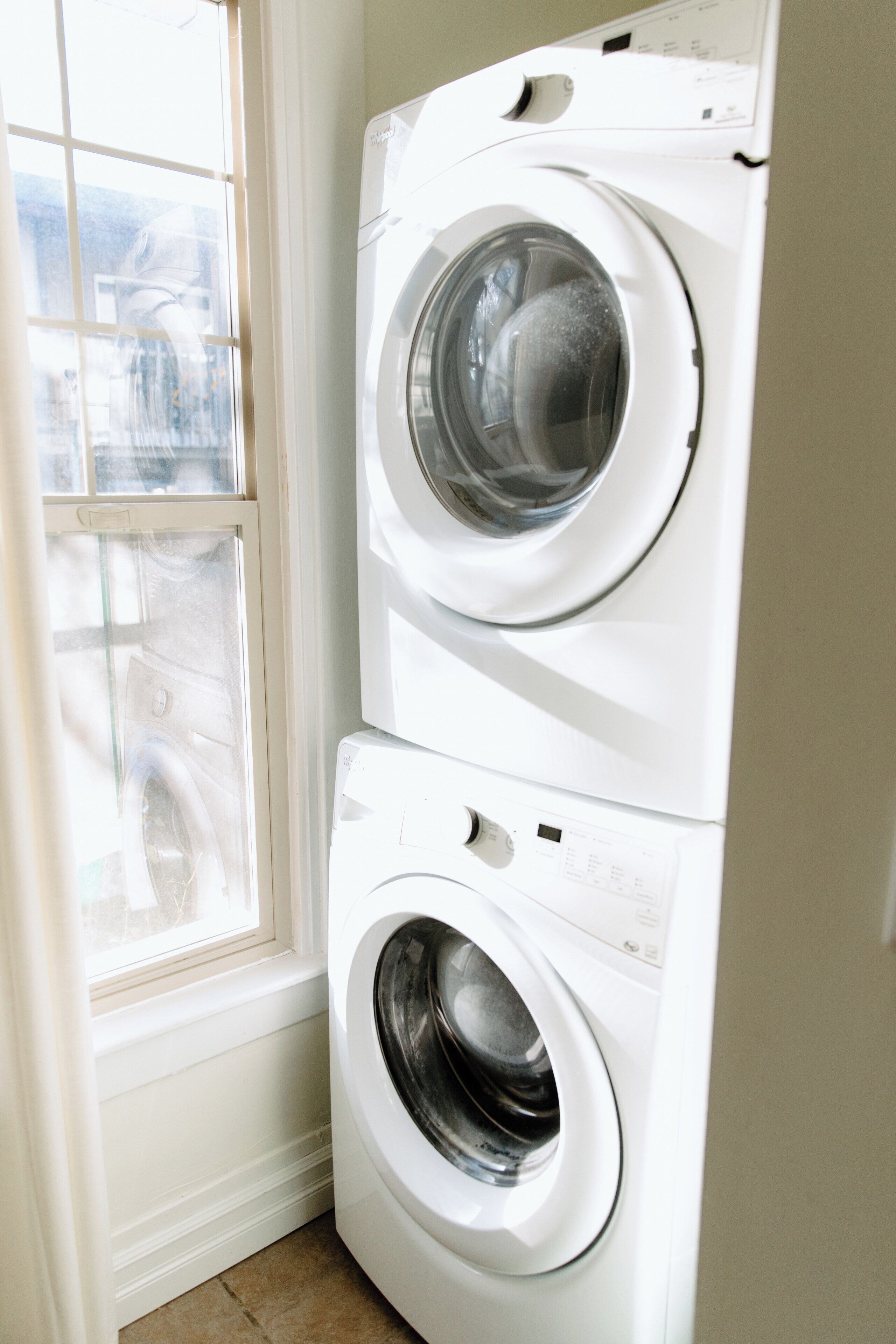 A stacked washer and dryer unit in a corner with a window.