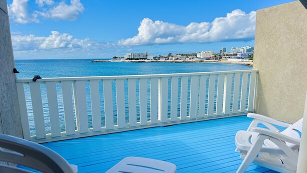 A balcony with white plastic chairs and a blue floor, overlooking a beach and cityscape. - Nice and cozy ocean front studio with private terrace. Short walk to beaches. (Beacon Hill)