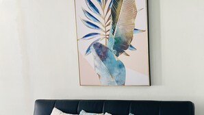 A black leather sofa with four decorative pillows, a framed artwork of tropical leaves, and a white tiled floor. - Nice and cozy ocean front studio with private terrace. Short walk to beaches. (Beacon Hill)