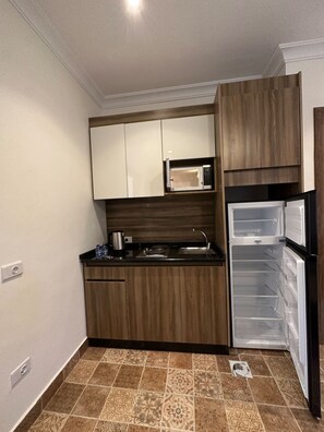 A compact kitchen with wooden cabinets, a microwave, a refrigerator, and a tiled floor.