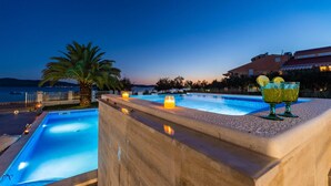 A swimming pool with a sunset view, a palm tree, and two cocktails on the edge.
