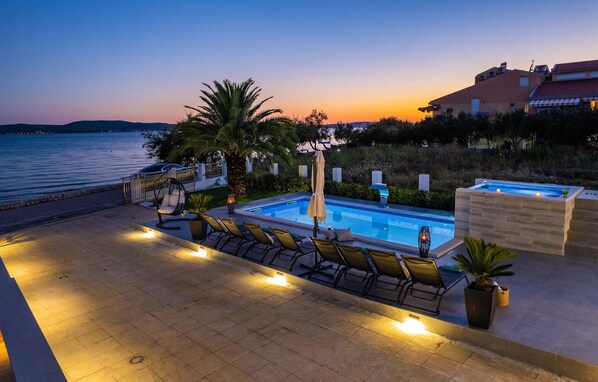 Un espace aménagé au bord de la piscine, avec des chaises longues, une piscine et une vue sur la mer au crépuscule.