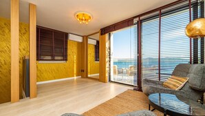 A modern living room with a large window, wooden floor, and a sofa with a throw pillow.