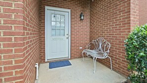 A brick building with a white door, a metal bench, and a small potted plant. - Tiger's Den on Dean In Auburn, 3BR/2.5BA 3 Miles from Jordan-Hare! (Auburn)