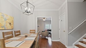 A dining area with a wooden table and chairs, a chandelier, and a painting on the wall. - Tiger's Den on Dean In Auburn, 3BR/2.5BA 3 Miles from Jordan-Hare! (Auburn)
