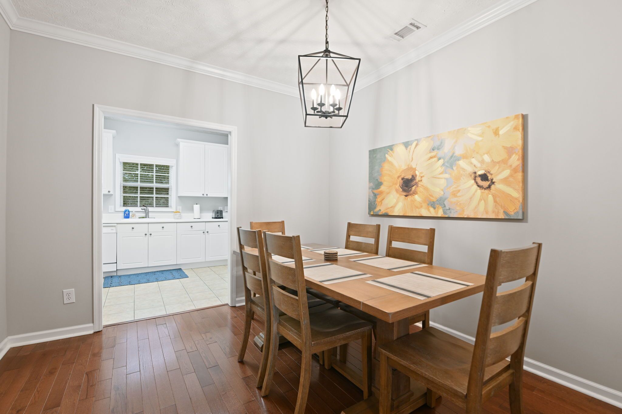 A dining area with a wooden table and chairs, a chandelier, and a sunflower painting on the wall.
