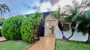 A pathway leading to a gated entrance with a white wall and palm trees. - Luxury Full House in Dorado, Puerto Rico (Dorado)