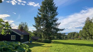 A house with a dark roof and a chimney, surrounded by a large green field and tall trees. - Pet friendly home in Tällberg (Tällberg)