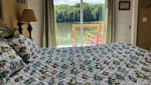 Une chambre avec un grand lit, une vue sur un lac, un fauteuil près de la fenêtre et une lampe sur la table de chevet.