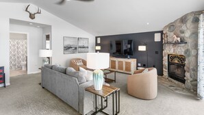 A modern living room with a stone fireplace, a sofa, a coffee table, and a television. - Escape to Hutchins Lake (Fennville)