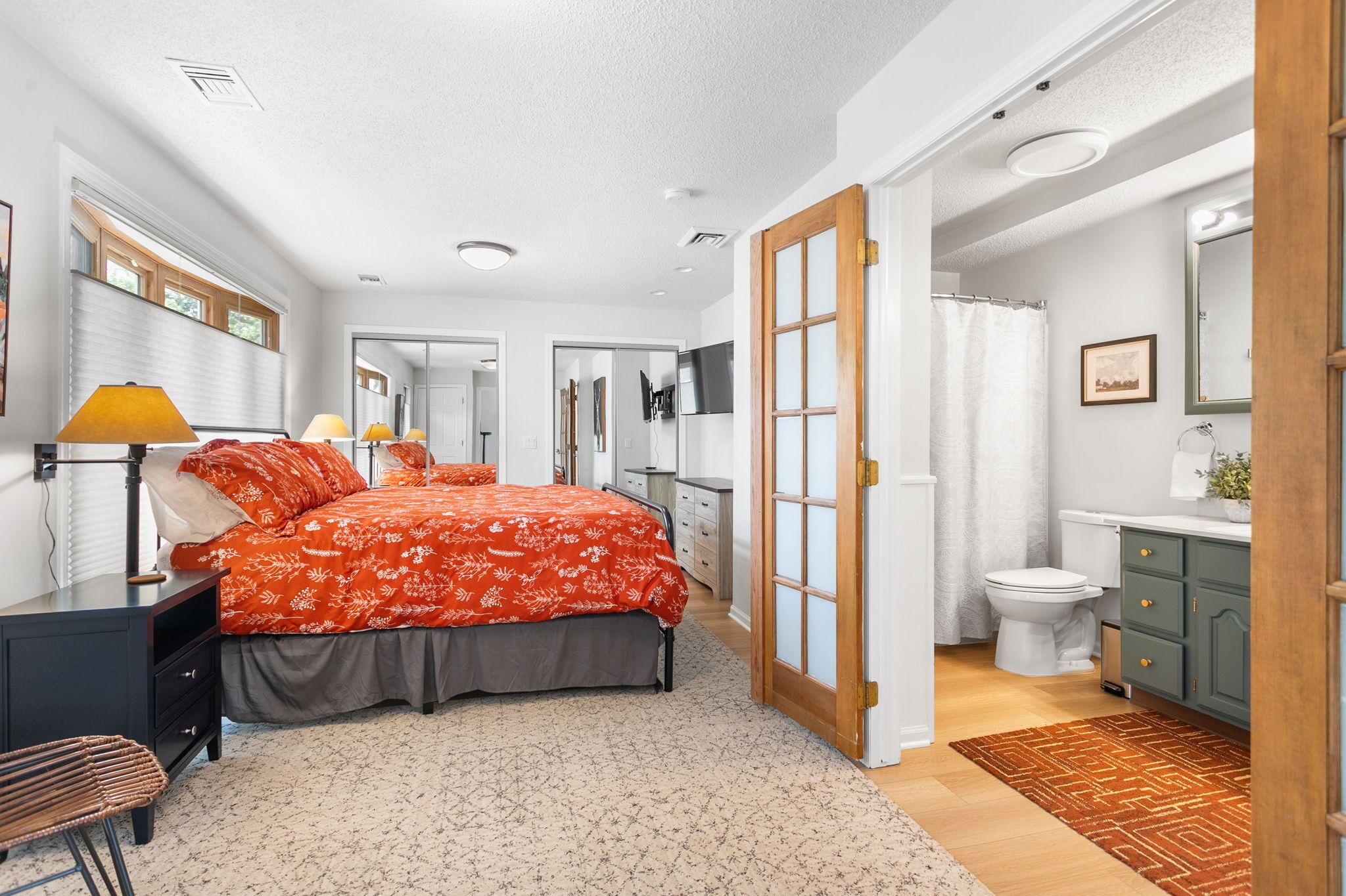 Ein Schlafzimmer mit einem Bett, Nachttischen, einem Sessel und einem Badezimmer mit Toilette und Waschbecken.