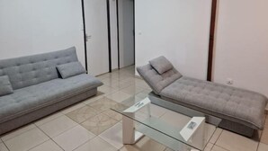 Un salon moderne avec un canapé gris, une table basse en verre et une petite banquette grise.