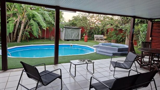 Une terrasse couverte avec une piscine, des sièges d’extérieur et une vue sur le jardin environnant.