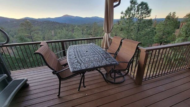 A wooden deck with a table and chairs, overlooking a mountainous landscape.
