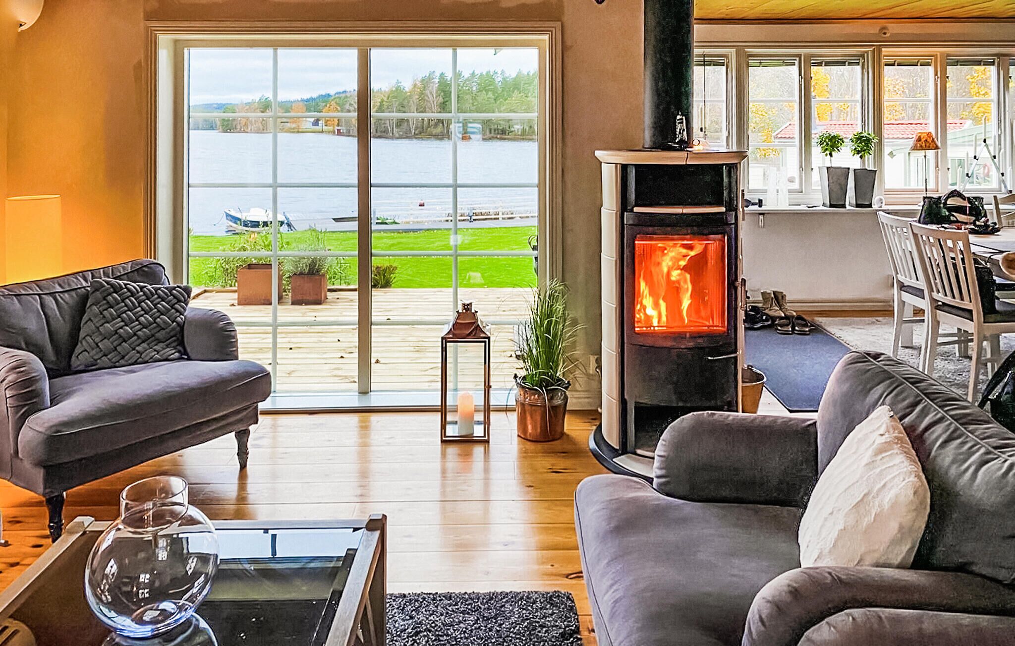 Ein gemütliches Wohnzimmer mit Kamin, einer Couch, einem Couchtisch und Blick auf einen See durch große Fenster.