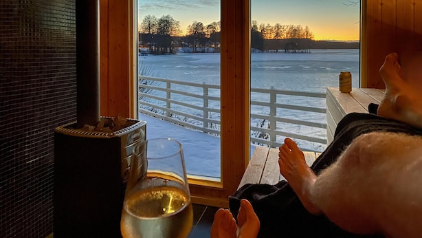 A person relaxing by a window with a view of a frozen lake and a sunset. - Nice home in Hjältevad with sauna (Hjältevad)