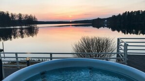 A hot tub on a deck overlooking a calm lake at sunset. - Nice home in Hjältevad with sauna (Hjältevad)