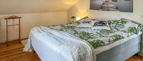 Quarto com cama, escada de madeira, quadro e luminária.