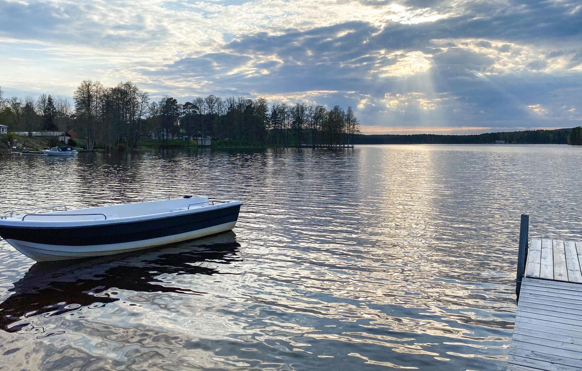 Ein ruhiger See mit einem Boot, das an der linken Seite vertäut ist, und einer Holzsteg, der sich ins Wasser erstreckt.