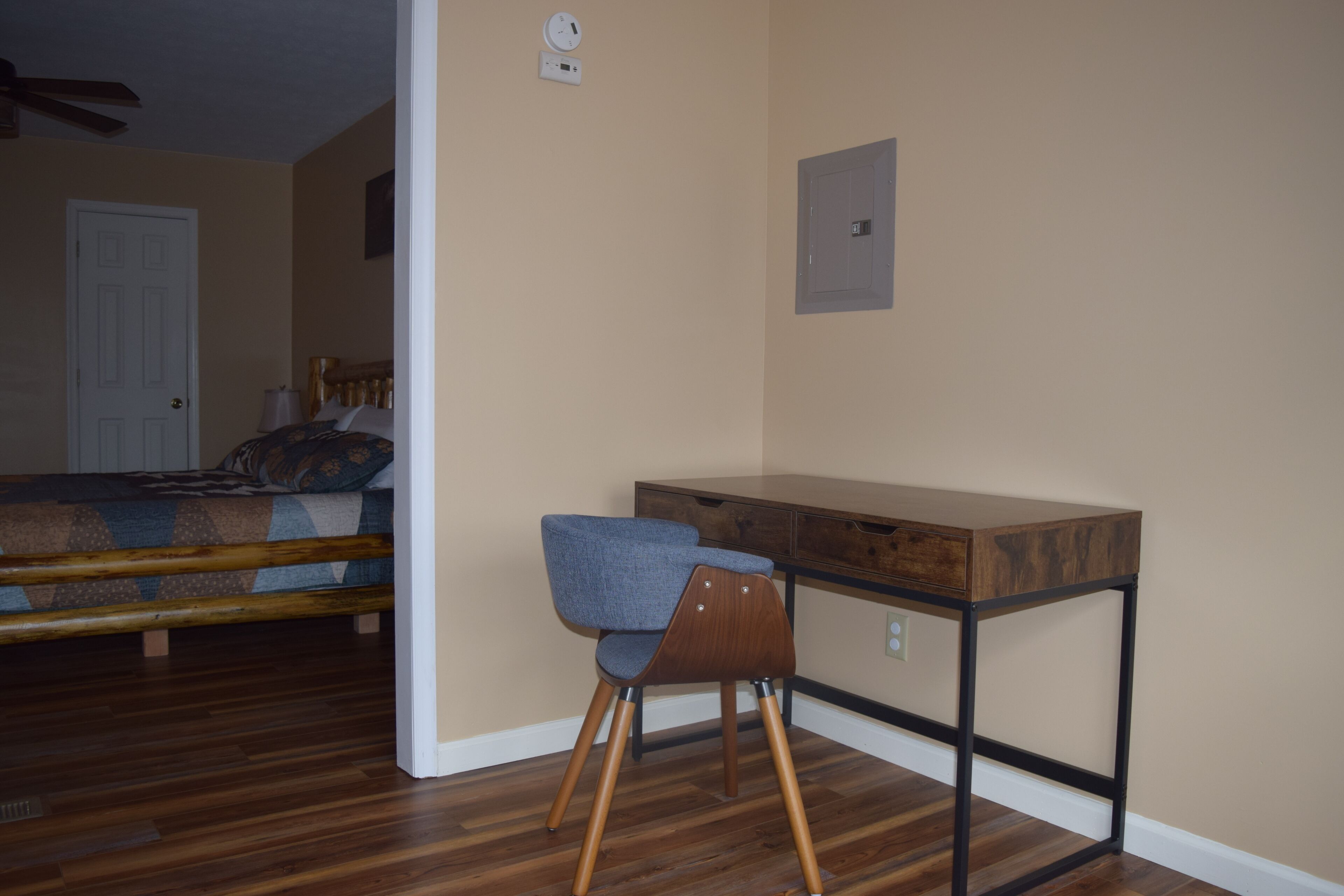 A bedroom with a wooden bed, a desk with a chair, and a door.