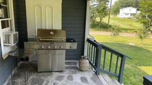 Eine überdachte Außenküche mit Grill, Steinboden und Blick auf ein Haus und Garten.