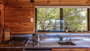 Une cuisine avec des murs en bois, un plan de travail en acier inoxydable, une cuisinière à gaz, une machine à café et une fenêtre donnant sur des arbres.
