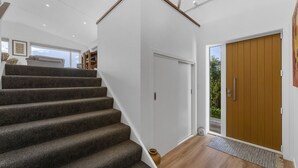 Un intérieur moderne avec un escalier recouvert de moquette, une porte en bois et une vue sur l’extérieur.