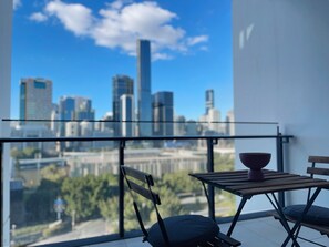 Enjoy a panoramic view of the city skyline from this balcony with a glass railing, wooden table, and comfortable chair.