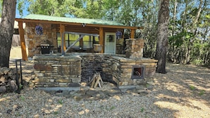 A rustic stone building with a chimney, a wooden deck, and a stone wall.