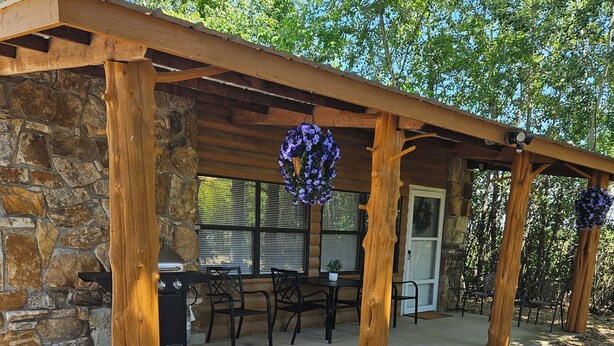 A covered patio area with stone walls, a grill, and outdoor seating.